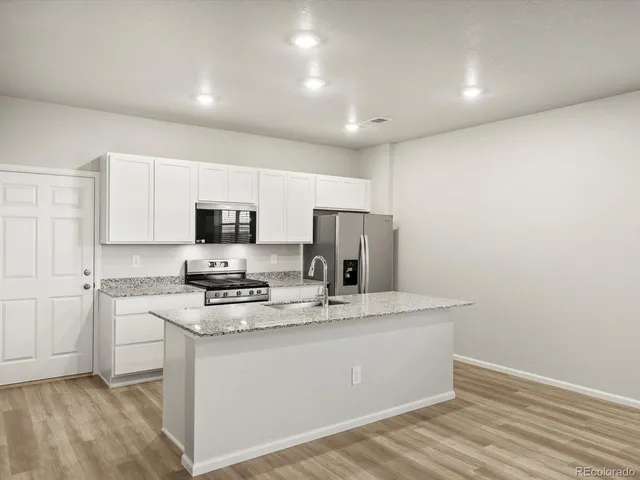 a kitchen with stainless steel appliances granite countertop a sink a stove a refrigerator with white cabinets and wooden floor