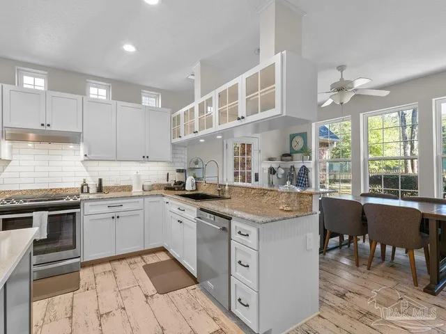 a kitchen with stainless steel appliances granite countertop a stove top oven a sink dishwasher and white cabinets with wooden floor