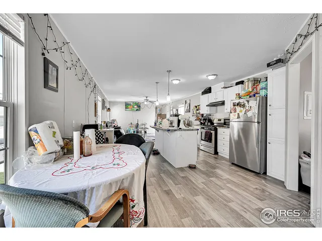 a open kitchen with stainless steel appliances kitchen island granite countertop a refrigerator a stove a sink dishwasher and white cabinets with wooden floor