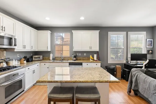 a kitchen with stainless steel appliances granite countertop a stove top oven a sink dishwasher and white cabinets with wooden floor