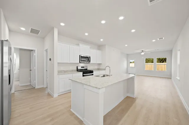 a large white kitchen with a stove a sink a refrigerator and white cabinets with wooden floor
