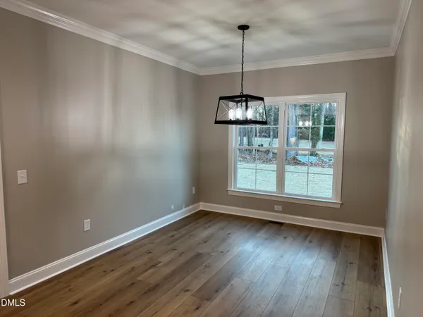 a view of an empty room with wooden floor kitchen view and a window