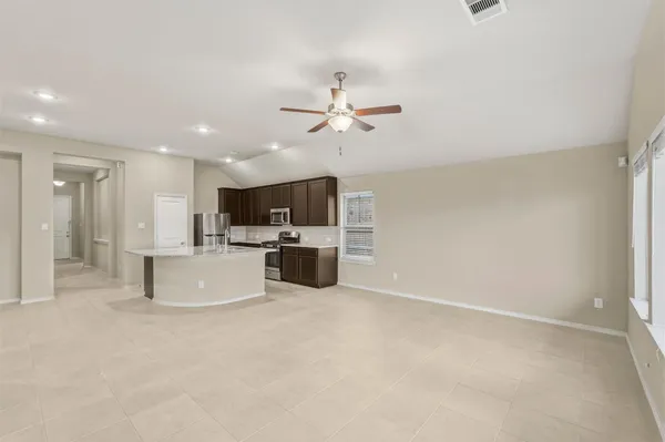 a large kitchen with kitchen island a stove a sink a refrigerator white cabinets and couches with wooden floor