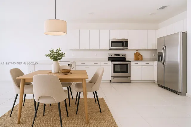 a kitchen with stainless steel appliances a stove a sink a microwave a refrigerator a dining table and chairs with wooden floor