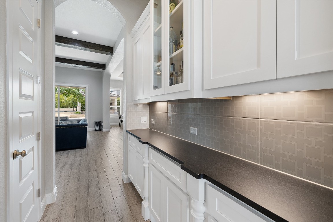 403 Woodside Terrace Austin, TX 78738 - Photo 11 of 38 Kitchen featuring tasteful backsplash, beamed ceiling, white cabinets, dark countertops, and glass insert cabinets