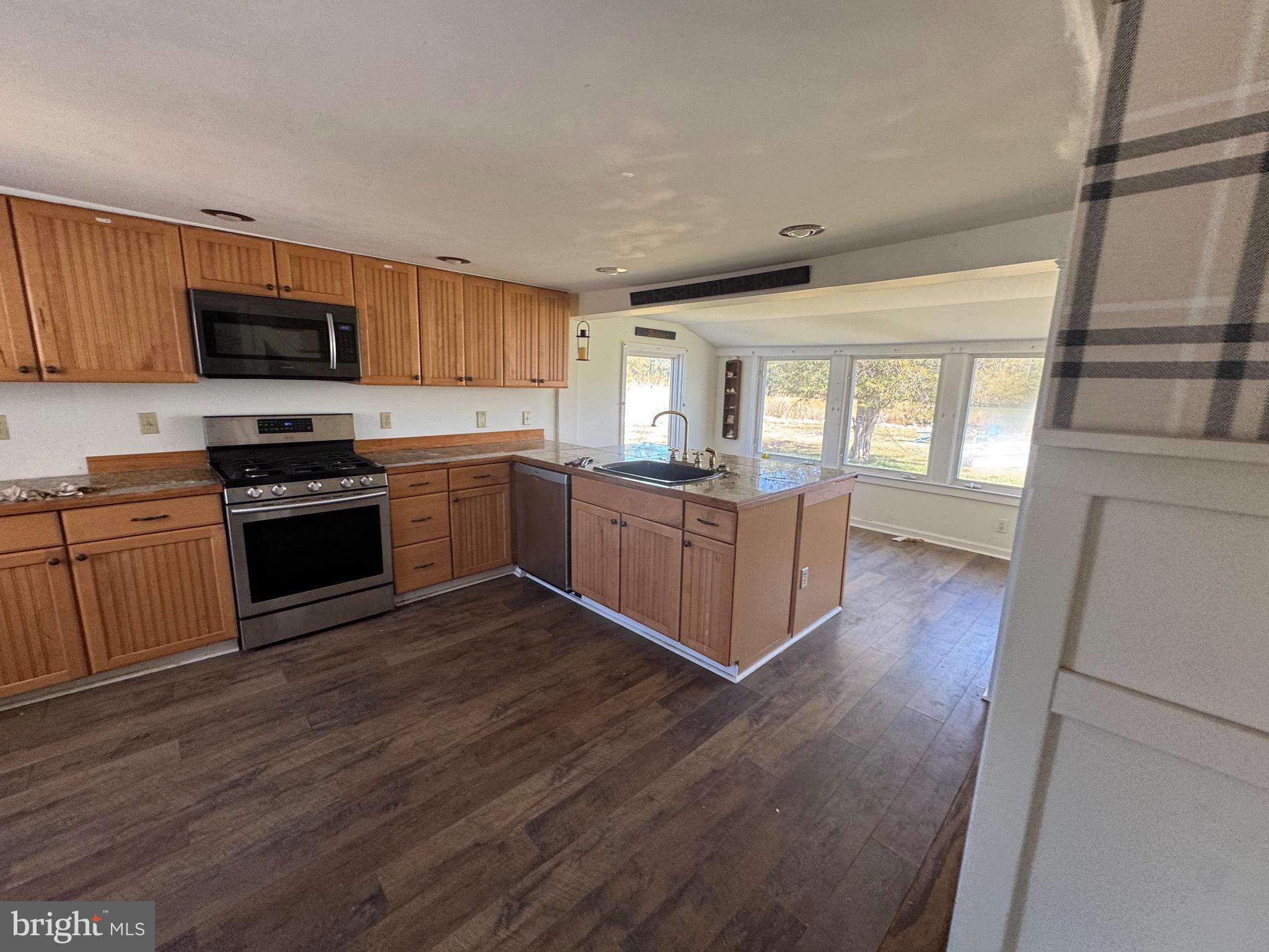 5511 Cassons Neck Road Cambridge, MD 21613 - Photo 18 of 24 a kitchen with stainless steel appliances kitchen island granite countertop wooden floors and white cabinets