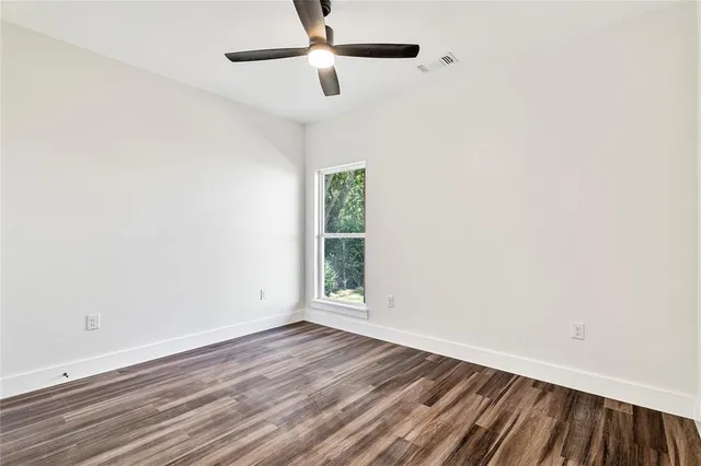 an empty room with wooden floor ceiling fan and windows