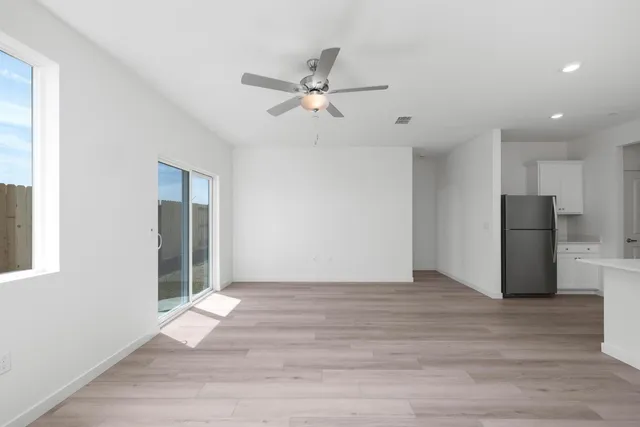 a view of an empty room with wooden floor and a ceiling fan