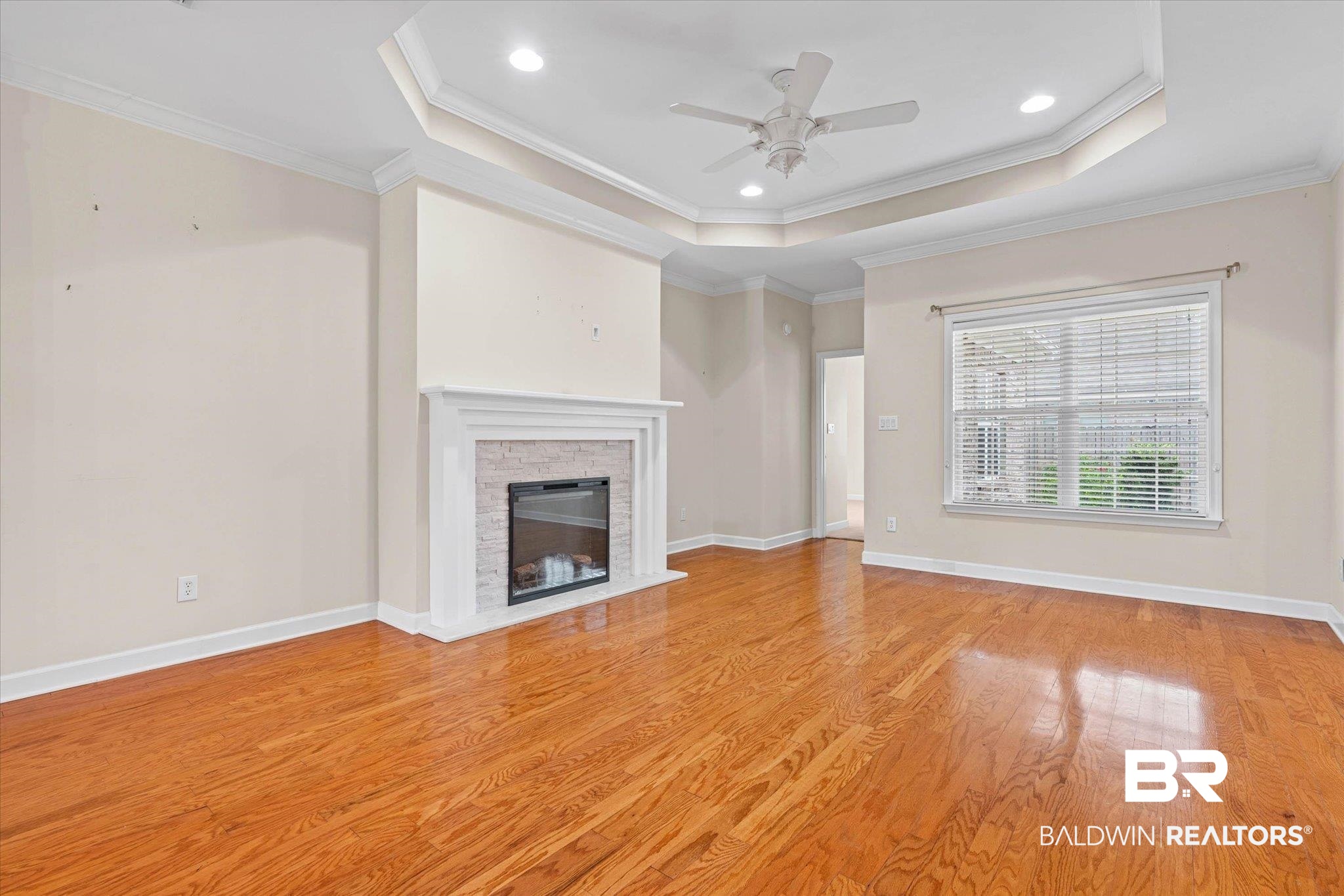 1003 Weatherby Street South Saraland, AL 36571 - Photo 6 of 31 Unfurnished living room with crown molding, a ceiling fan, a tray ceiling, a stone fireplace, and light wood finished floors