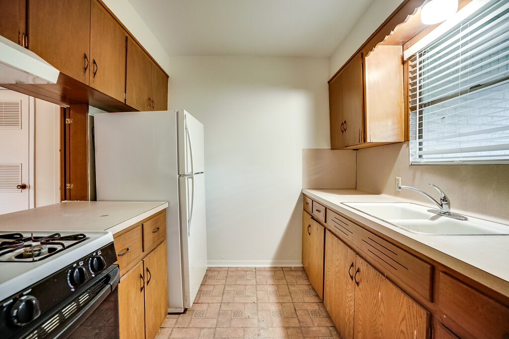 3707 Tom Green Street, Unit 2 Austin, TX 78705 - Photo 2 of 14 Kitchen with brown cabinets, range with gas stovetop, light countertops, freestanding refrigerator, and under cabinet range hood