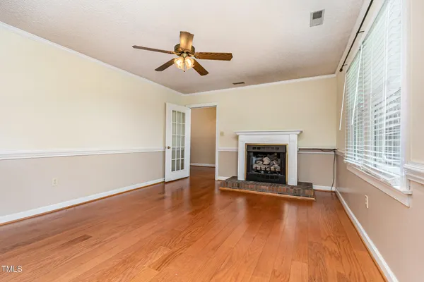 a view of an empty room with wooden floor fireplace and a window
