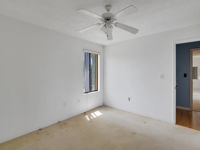 an empty room with chandelier fan and windows
