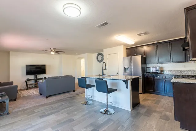 a kitchen with stainless steel appliances kitchen island granite countertop a refrigerator a stove a sink a dining table and chairs with wooden floor
