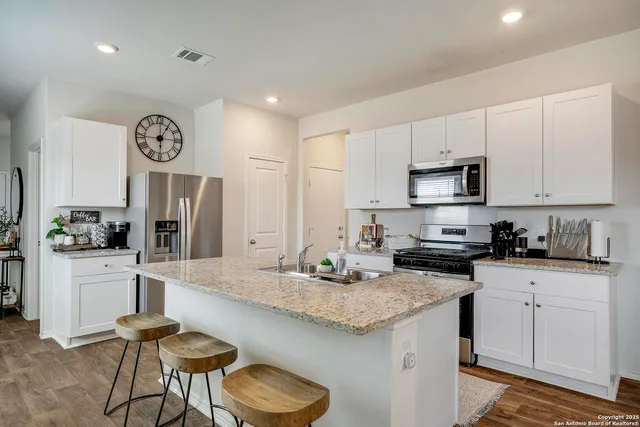 a kitchen with stainless steel appliances granite countertop a kitchen island a stove a refrigerator a stove a dining table and chairs with wooden floor
