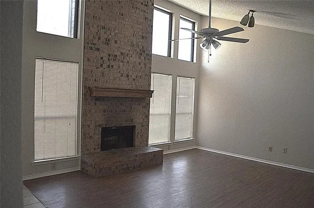 an empty room with wooden floor fireplace and windows