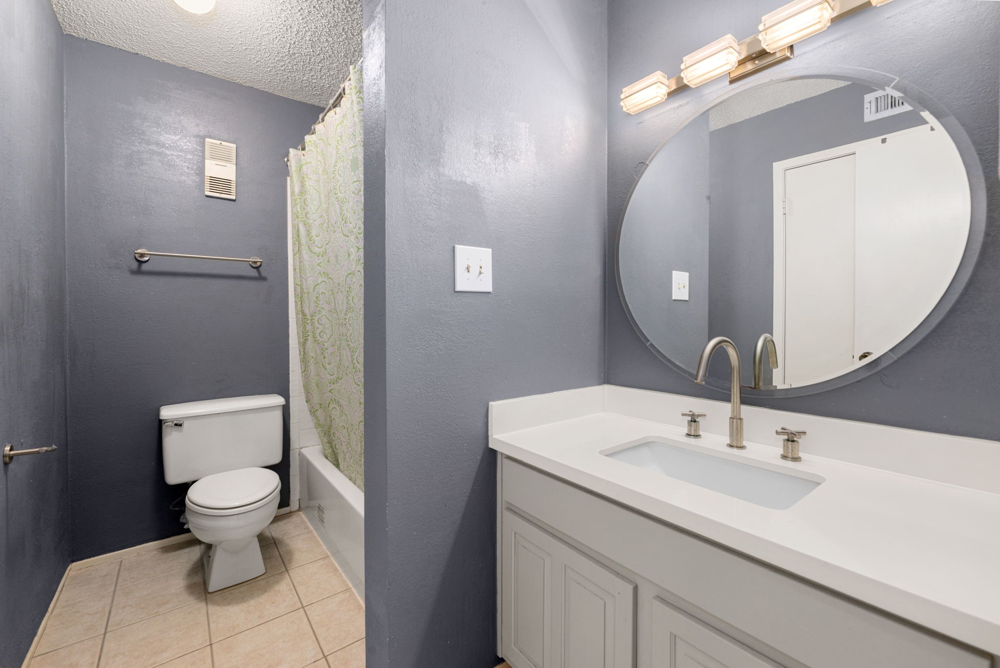 3200 South Gessner Road, Unit 228 Houston, TX 77063 - Photo 11 of 18 The primary bath features a white vanity with quartz countertop, undermount sink, brushed nickel fixtures, a stylish round mirror with Hollywood-style lighting, tile flooring, and a tub/shower combo, clean, bright, and move-in ready!