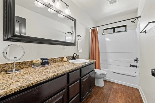 a bathroom with a granite countertop sink a toilet a mirror and shower