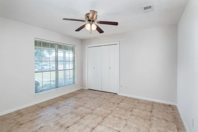 an empty room with chandelier fan and windows