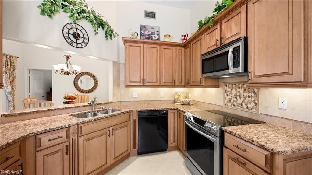 577 Beachwalk Circle, Unit R202 Naples, FL 34108 - Photo 10 of 44 Kitchen with stainless steel appliances, light stone countertops, wood finish cabinetry, and a chandelier