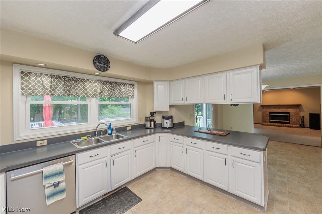 4123 Baird Road Stow, OH 44224 - Photo 13 of 47 Kitchen with white cabinets, sink, a fireplace, stainless steel dishwasher, and light tile patterned flooring
