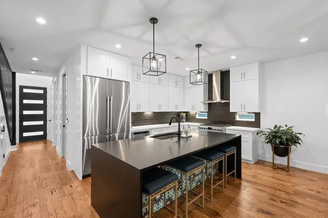 a kitchen with stainless steel appliances granite countertop a refrigerator a sink dishwasher a stove and a dining table with wooden floor