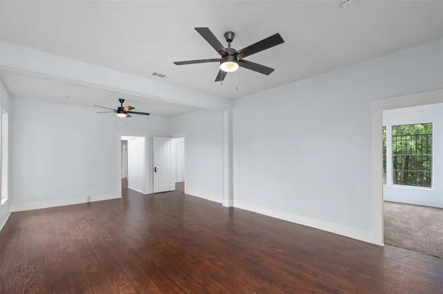 a view of an empty room with wooden floor and a ceiling fan