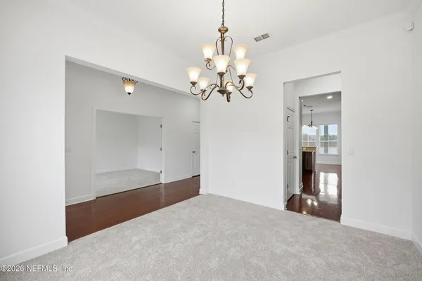 a view of an empty room with chandelier fan and kitchen view