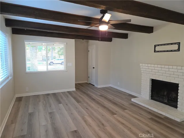 a view of an empty room with wooden floor fireplace and a window