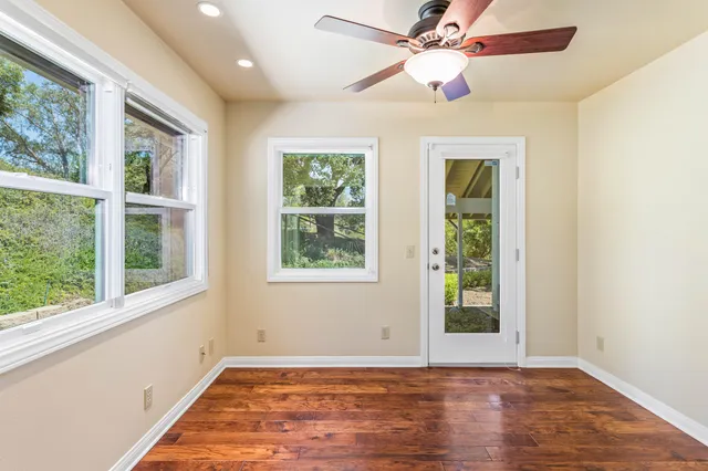 an empty room with wooden floor fan and windows