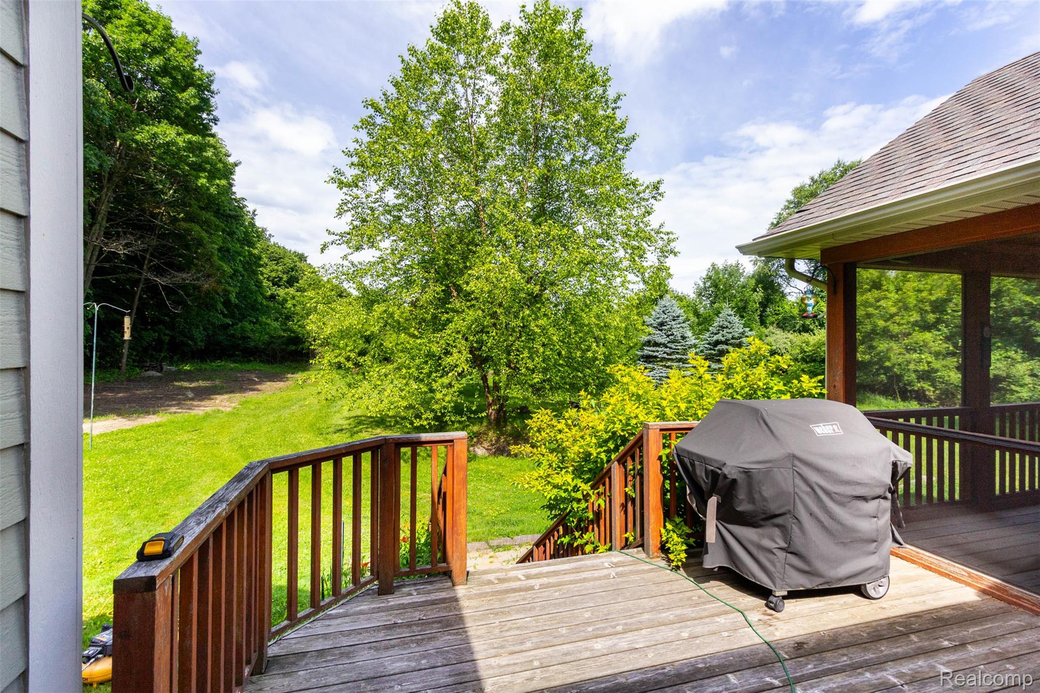 9887 Hadley Road Clarkston, MI 48348 - Photo 30 of 56 Expansive wooden deck with coordinating railings, featuring a covered outdoor area and steps leading to a large grassy lawn