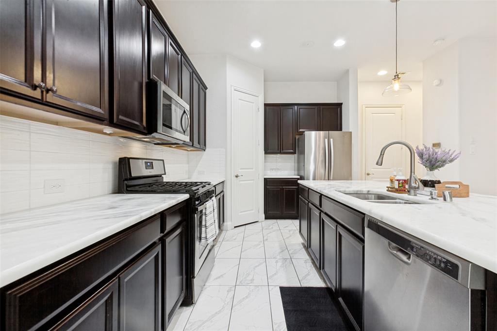 605 Ansley Way Allen, TX 75013 - Photo 13 of 28 Contemporary kitchen featuring dark wood cabinetry, white countertops, stainless steel appliances, a tile backsplash, and tile flooring