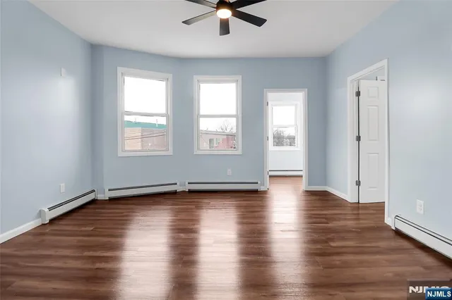 an empty room with wooden floor chandelier fan and windows