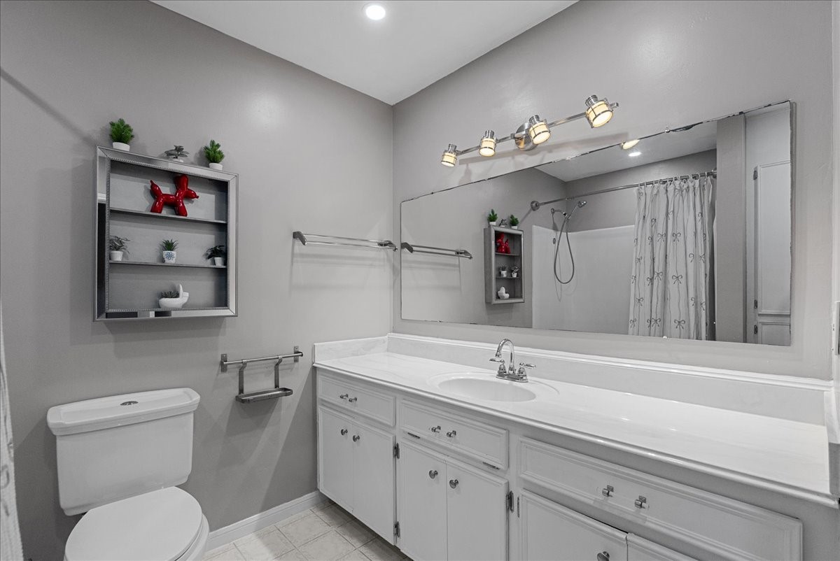 883 Silverpines Road Houston, TX 77062 - Photo 25 of 38 This bathroom features a clean, modern design with a large vanity, ample counter space, and a wide mirror. It includes a shower-tub combo with a curtain, along with open shelving for decor and storage. The lighting is bright, complemented by neutral wall colors.