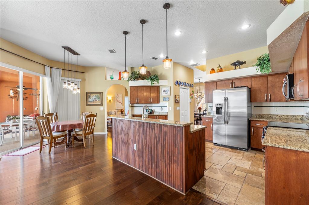 3051 Waterfall Drive Spring Hill, FL 34608 - Photo 60 of 74 a large kitchen with stainless steel appliances kitchen island granite countertop a table chairs and a wooden floor