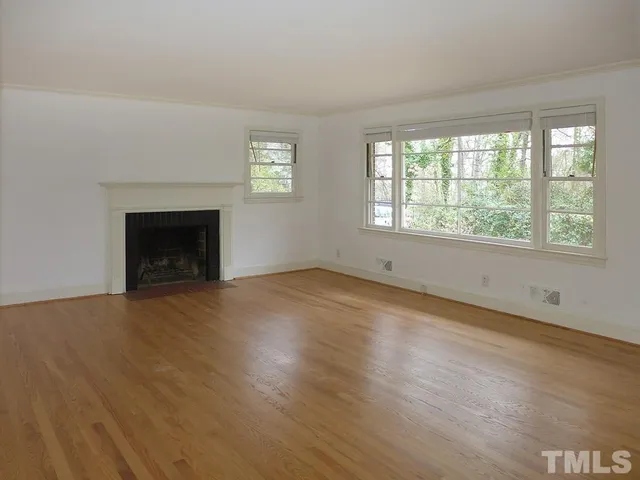 an empty room with wooden floor fireplace and windows