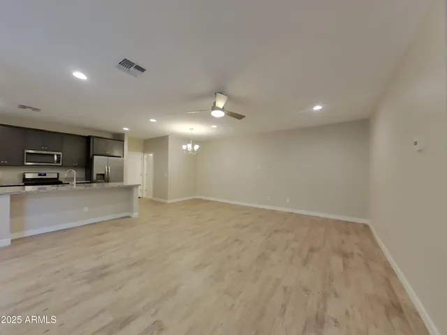 a view of an empty room with kitchen and window