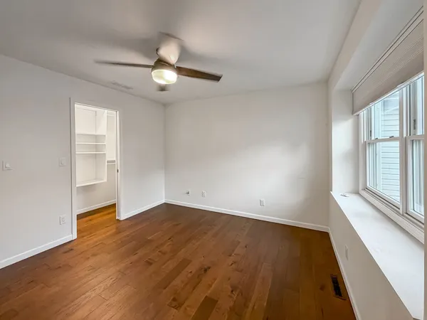 an empty room with wooden floor fan and windows