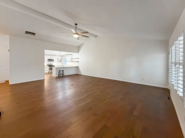 an empty room with wooden floor ceiling fan and windows