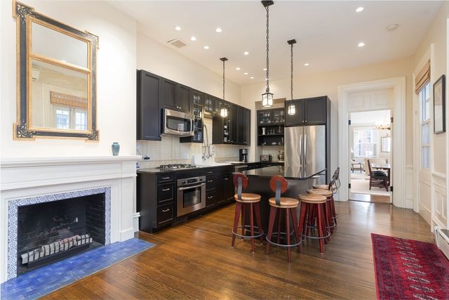 a kitchen with stainless steel appliances granite countertop a stove top oven a refrigerator a kitchen island a dining table and chairs with wooden floor