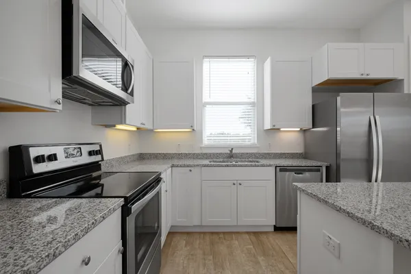 a kitchen with kitchen island granite countertop a stove a sink and white cabinets with wooden floor