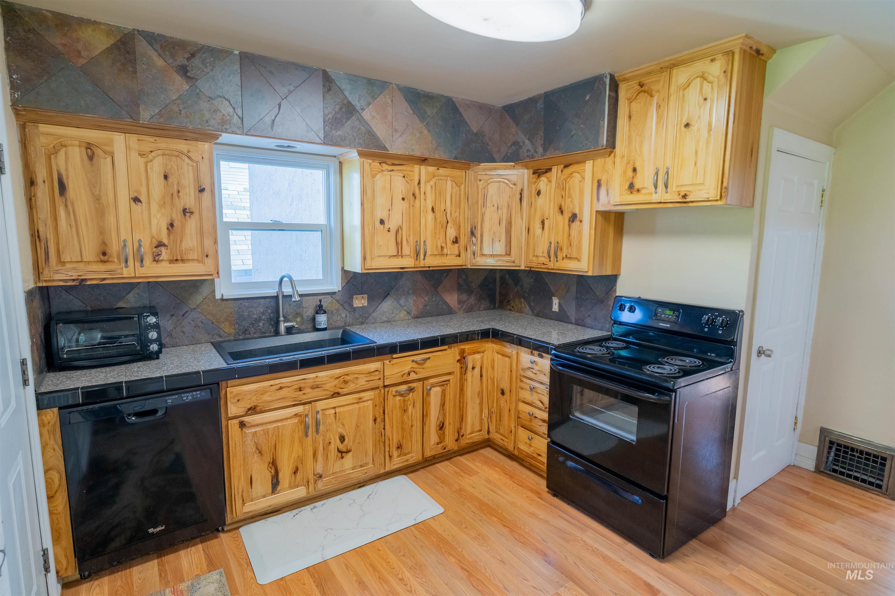 1212 14th Street Lewiston, ID 83501 - Photo 12 of 50 Kitchen featuring black appliances, decorative backsplash, tile counters, and light wood-type flooring