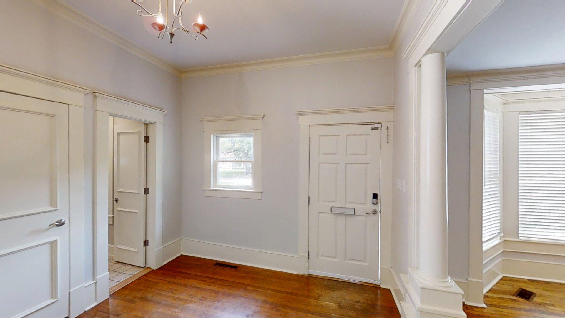 219 F Street Southwest Ardmore, OK 73401 - Photo 2 of 58 Hardwood flooring, classic crown molding, white paneled doors, column accent, and a bay window with blinds