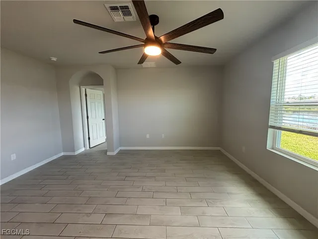 an empty room with chandelier fan and windows