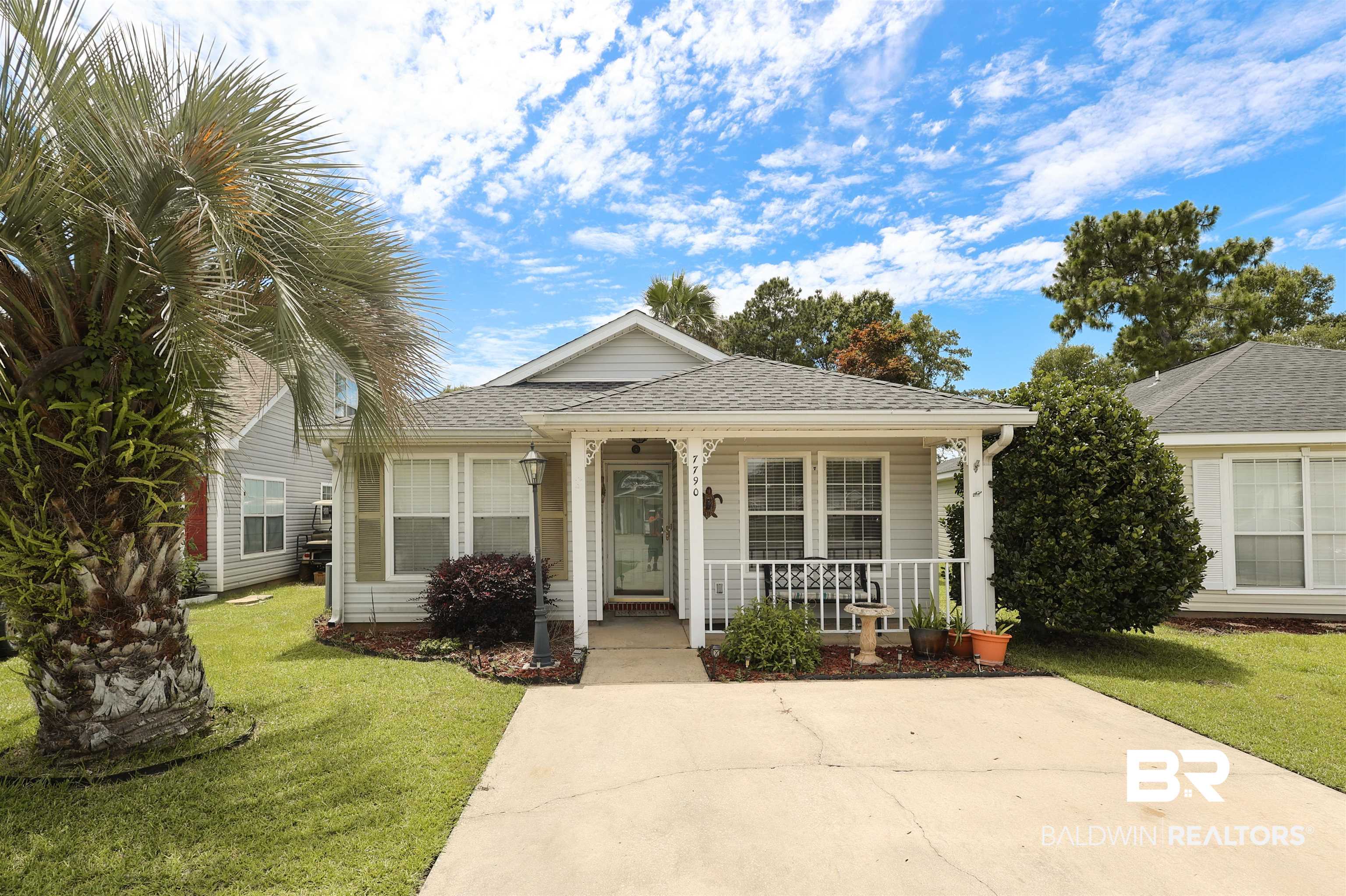 7790 Audubon Drive Foley, AL 36535 - Photo 1 of 39 Single-story residence featuring light-colored siding, a covered front porch with white railings, a concrete driveway, and a manicured lawn with mature landscaping