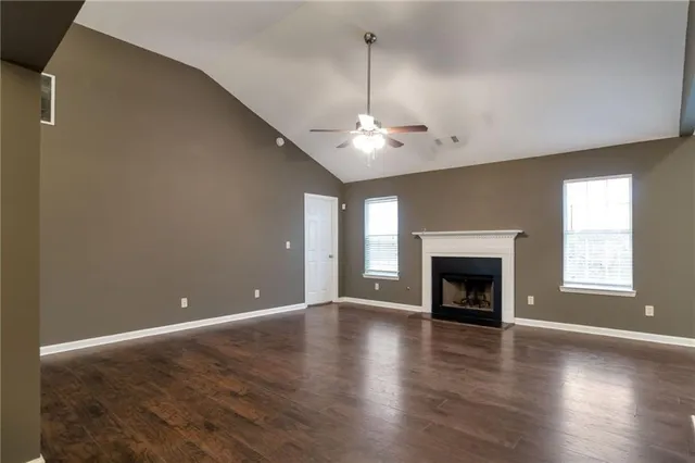 an empty room with wooden floor fireplace and windows