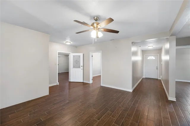 a view of an empty room with wooden floor and a ceiling fan