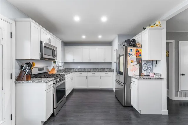 a kitchen with stainless steel appliances granite countertop a stove top oven a refrigerator a sink and dishwasher with wooden floor