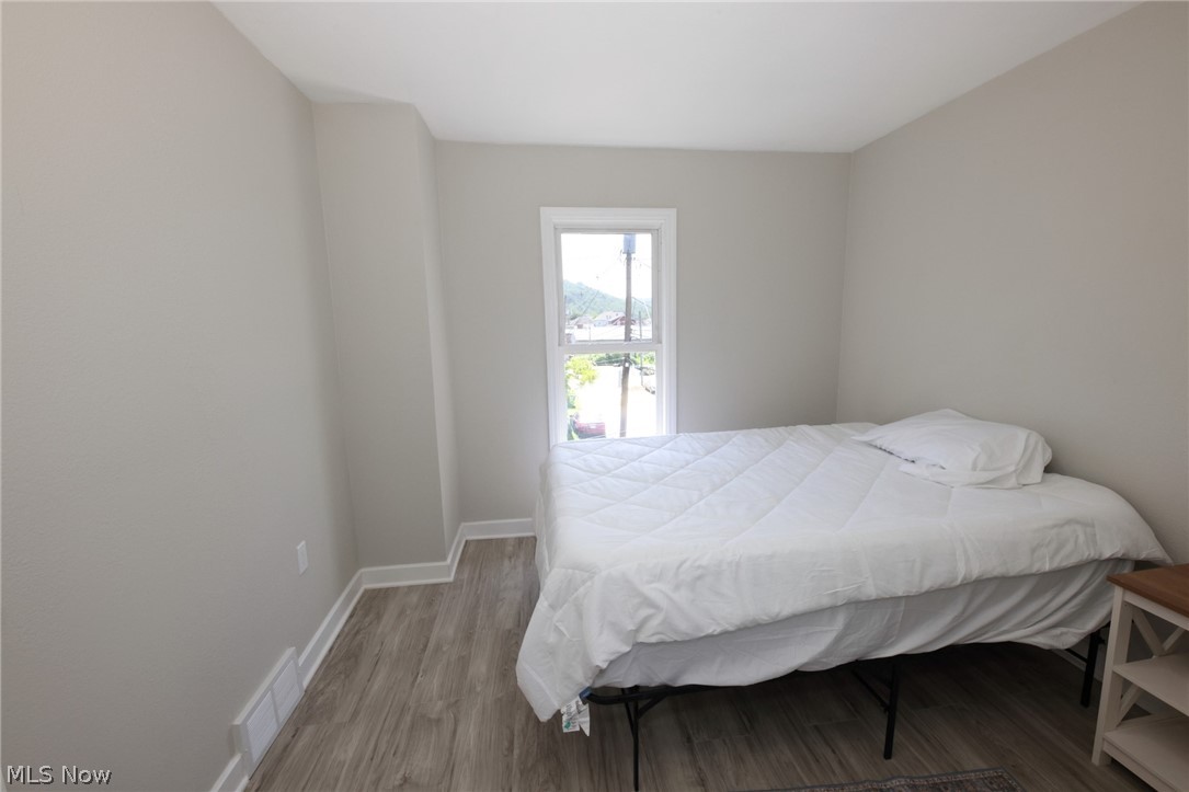 416 5th Street Chester, WV 26034 - Photo 16 of 24 Bedroom featuring light gray wall paint, wood-finish flooring, white baseboards, and a window with white trim