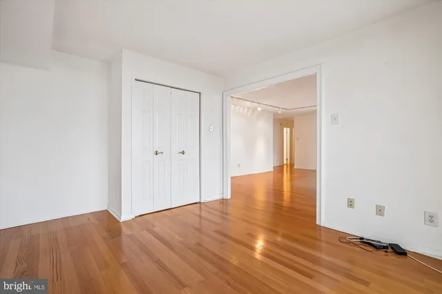 a view of an empty room and kitchen with wooden floor