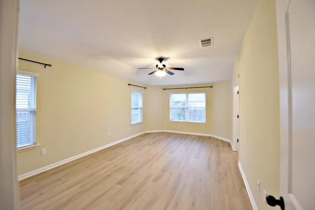 an empty room with wooden floor chandelier fan and windows
